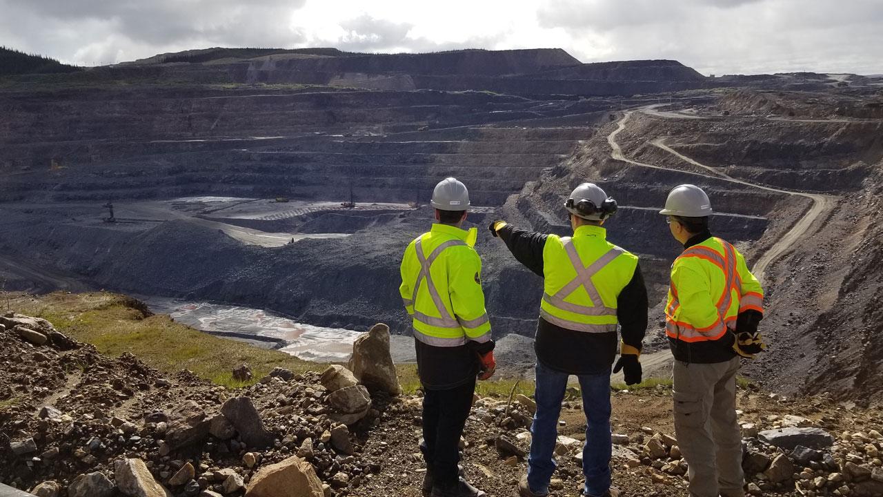 Three people in PPE look out over a mine